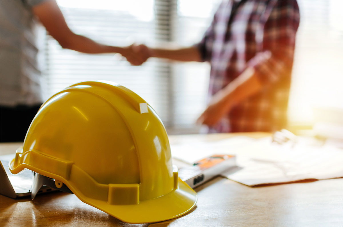 HomePage-BG shaking hands behind yellow hard hat
