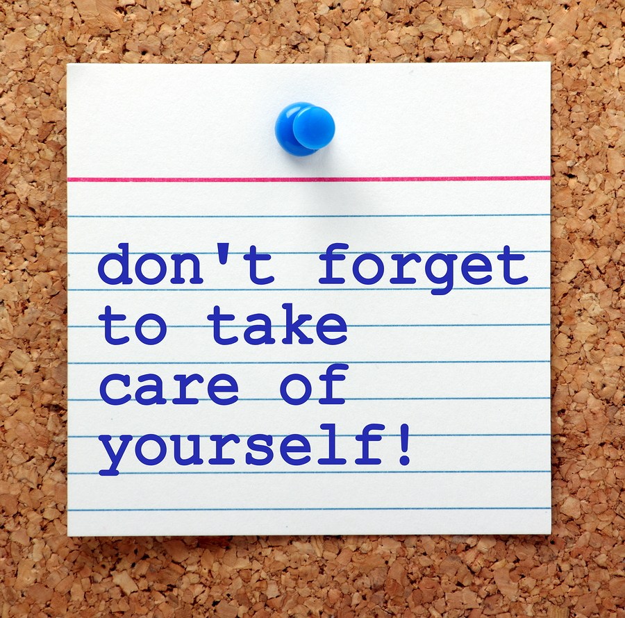 The words Don't Forget to Take Care of Yourself on a note card pinned to a cork notice board as a reminder to look after our own mental and physical health